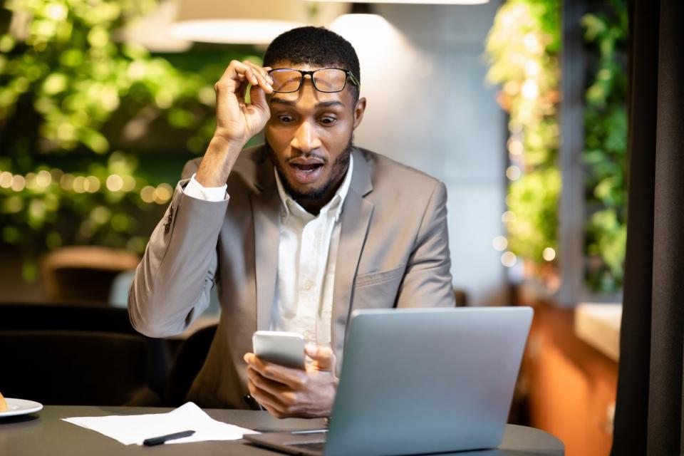 Investor taking off glasses while looking at phone surprised